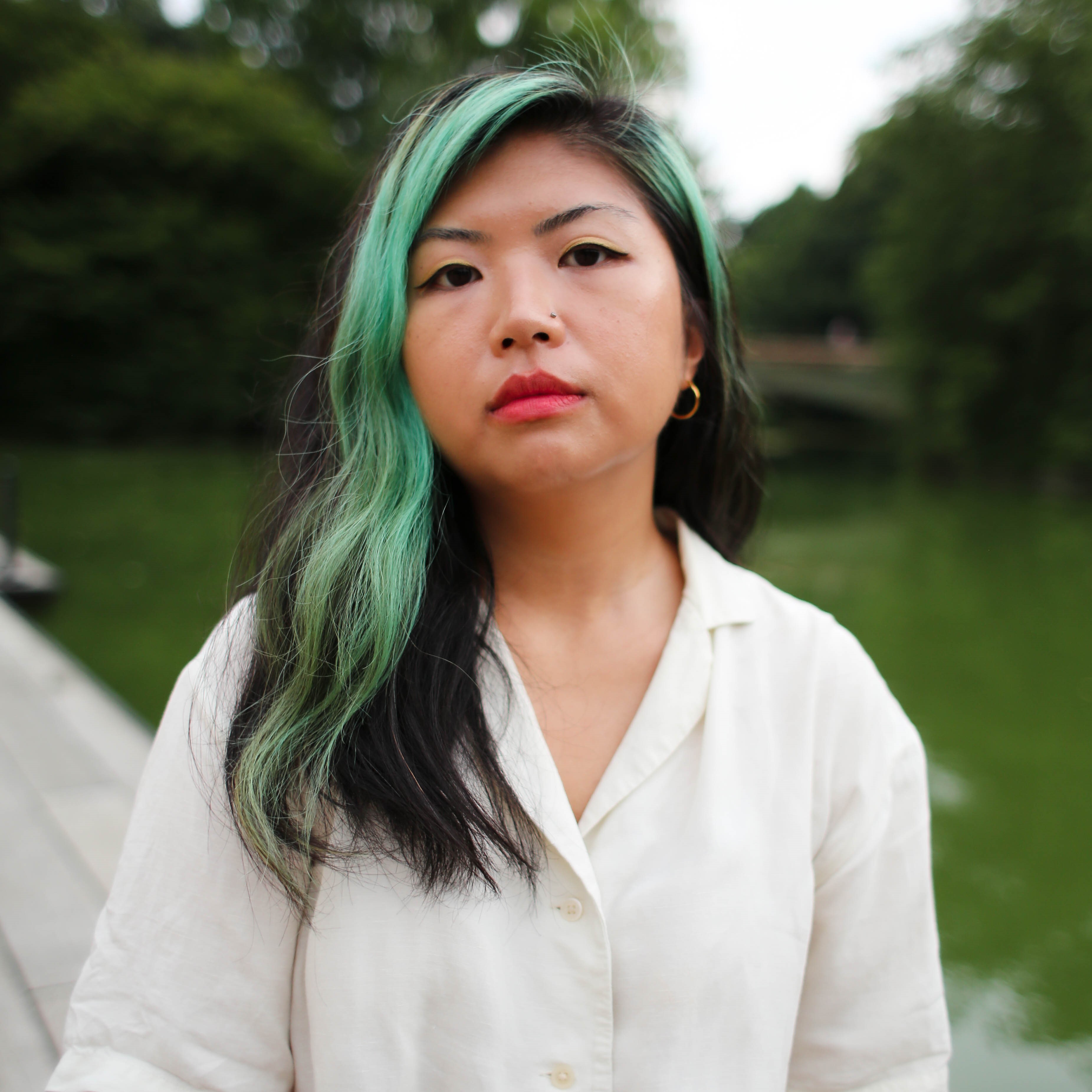 a Korean American with a streak of green hair and off-white blouse